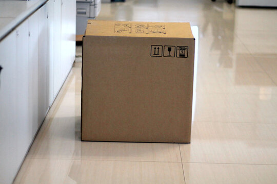 Cardboard Shipping Box On Office Floor With Fragile Symbols For Delivery, Storage And Moving