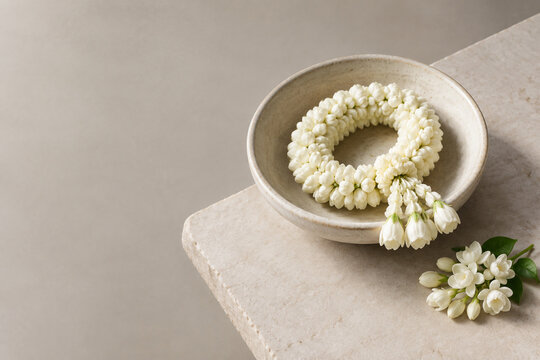Ceramic bowl with sampaguita garland on stone slab, premium understated mood