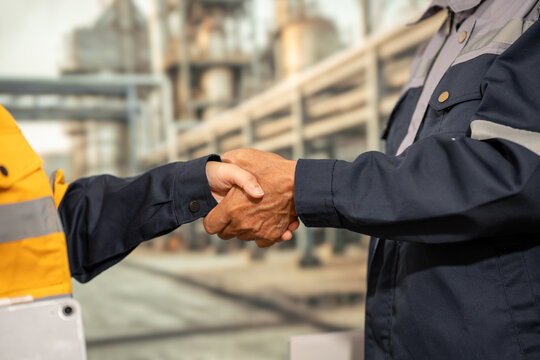 Close-up of industrial workers shaking hands at a factory site, showing partnership, agreement, teamwork, and professional cooperation.