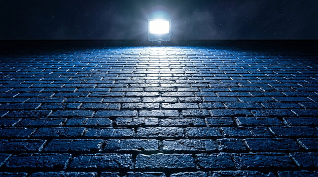 Bright outdoor floodlight illuminating a textured dark blue brick surface at night from a low angle, highlighting masonry details under a dark starry sky with high contrast.