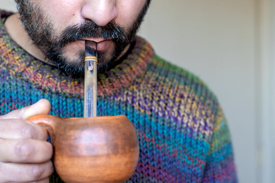 Close-up of the mouth of a bearded man holding and drinking from a hot cup of yerba mate blend, a traditional South American beverage