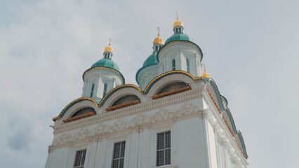 Low angle view of ornate white church featuring teal domes with gold crosses. Soft daylight highlights intricate stonework arched windows against pale sky © VeNN