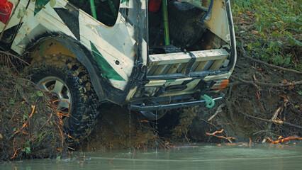 White green camouflage off road vehicle in thick mud beside shallow water, rugged tires caked in dirt, water dripping from undercarriage, natural daylight, outdoor adventure setting, muddy racing.. © VeNN
