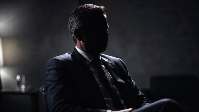 Business executive sitting in shadow during a serious interview, representing leadership, privacy, power and confidential corporate matters