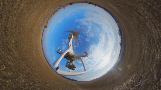 Little planet effect drone footage showing quadcopter flying over autumn landscape under blue cloudy sky.
