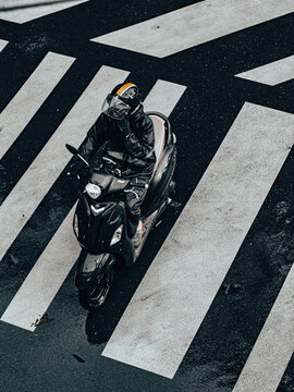 Aerial View of Motorcyclist in Black Raincoat and Helmet Crossing Wet Zebra Crosswalk