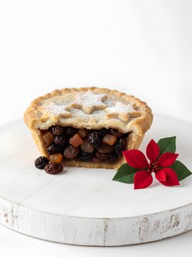 Traditional Christmas mince pie with a star-shaped crust on top, dusted with powdered sugar. The interior is visible, revealing a rich mix of dried fruits like raisins and candied orange peels. 