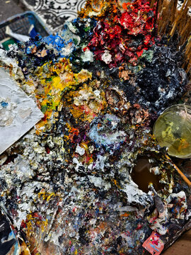 Vibrant messy artist palette covered in glossy paint, scattered brushes and tubes, dried paint