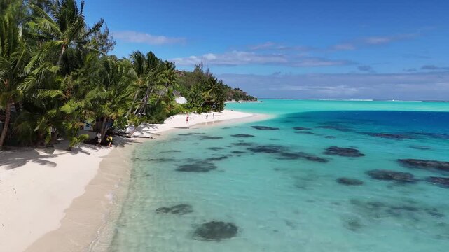 Wide stationary aerial drone shot showcasing the pristine white sands of Matira Beach, palm trees, and vibrant shallow coral reefs in Bora Bora, French Polynesia