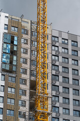 Construction of a modern high-rise building with a vibrant yellow crane against a cloudy sky © beholdereye