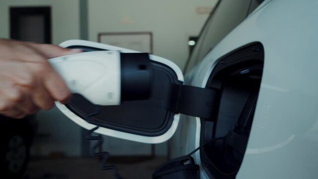 Person plugging in EV charging cable to white electric vehicle for sustainable energy transport.