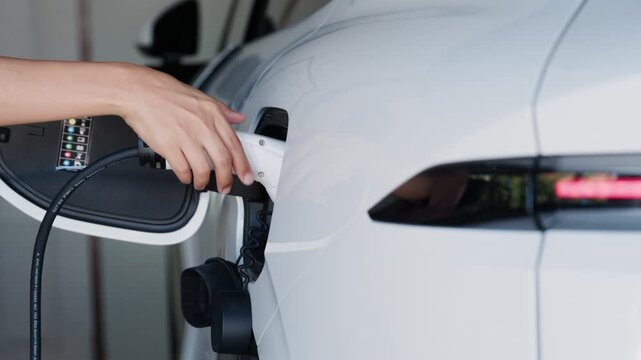Person plugging in EV charging cable to white electric vehicle for sustainable energy transport.
