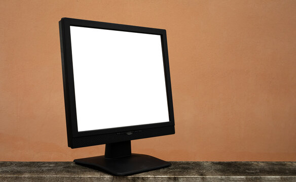 Side view, black computer screen with blank white screen, on orange wall background.