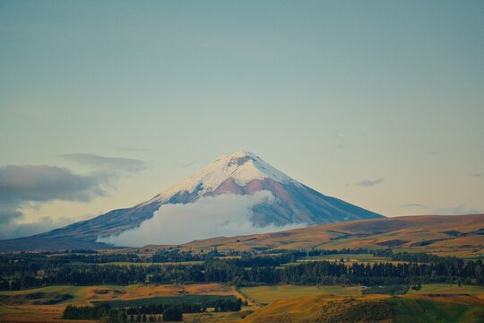 Cotopaxi volcano peak with snow and clouds over rolling hills in Ecuador