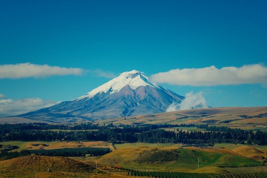 Cotopaxi volcano peak with snow and clouds over rolling hills in Ecuador