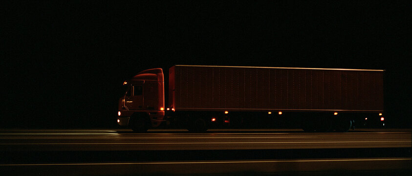 Red Semi-Truck Driving on Highway at Night with Illuminated Taillights and Headlights