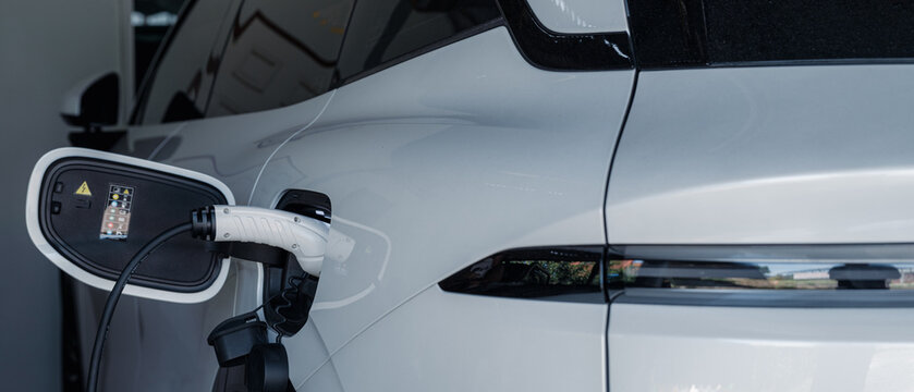 Person plugging in EV charging cable to white electric vehicle for sustainable energy transport.