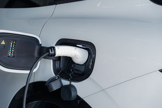Person plugging in EV charging cable to white electric vehicle for sustainable energy transport.