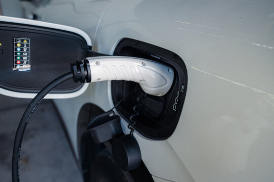 Person plugging in EV charging cable to white electric vehicle for sustainable energy transport.