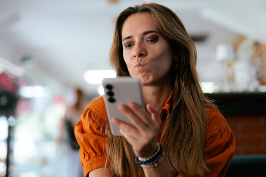 Woman Checking Her Phone Displeased At Restaurant Table. Annoyed young woman looks at her smartphone screen while sitting indoors