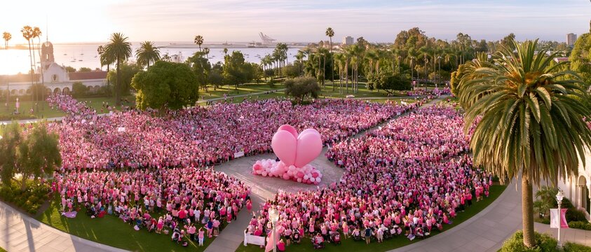 Mass gathering of people in pink attire at waterfront park under sunset