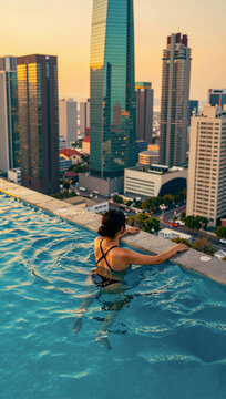 Woman swims in rooftop pool overlooking city skyline at sunset.