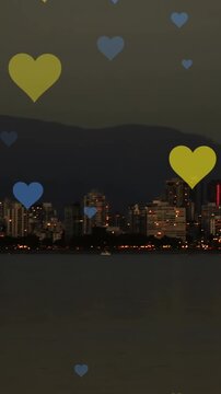 Animation of yellow and blue hearts floating over night cityscape