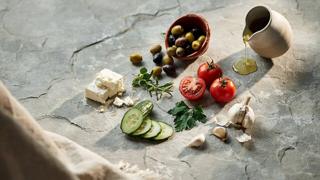 Assortment of feta cheese olives tomatoes and herbs on a textured surface