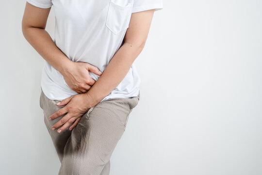 Close-up of a woman experiencing urinary incontinence with wet pants holding her lower abdomen and groin area. Concept of bladder control issues, urinary tract infection, and female health problems.