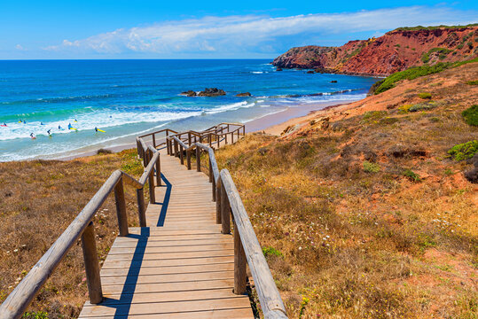 Staircase to the beach along the rocky algarve coast. Group of surfers practicing surfing.