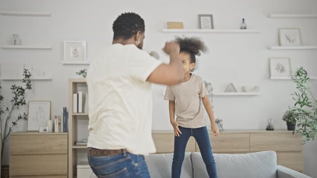 Father and his young daughter dance and spin playfully together in a bright modern living room, laughing through a joyful and active family moment at home.