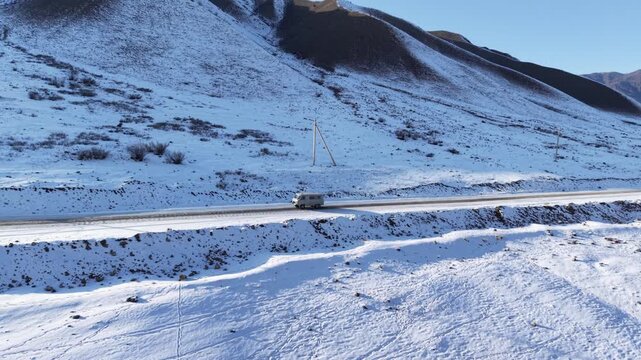 Aerial tracking shot following van driving on empty mountain road in snowy landscape, Kazakhstan