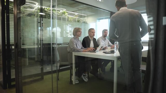 A view through a glass partition shows a modern, busy office interior. Job interview process is in office. Human resources, meeting and group of hiring candidates for vacancy