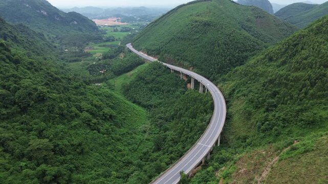 Cinematic drone arc shot of a scenic interprovincial national highway viaduct bridge in Vietnam. Aerial view of modern road infrastructure with traffic nestled amidst beautiful green mountains.