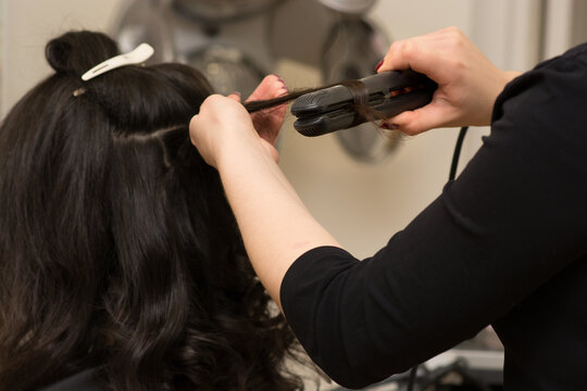 Hair stylist making ringlets to brunette woman. Hairdresser working with beautiful woman hair in hairdressing salon.
