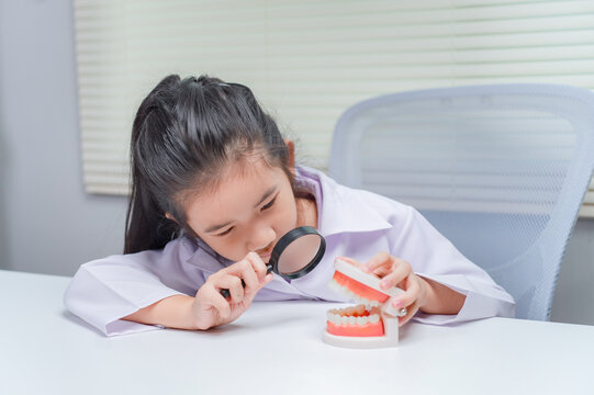 Little girl using magnifying glass inspecting toy teeth for dental health checkup in educational healthcare setting	