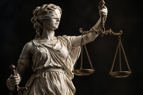 Classical statue of Lady Justice with scales on dark background.