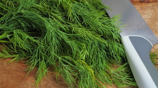 Close-up of fresh dill herbs on a wooden cutting board with a knife nearby, ready for chopping. High quality 4k footage