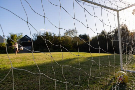 soccer net view of teenage boy striking soccer ball into net at sunset