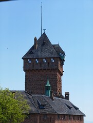 Red stone medieval castle tower with a roof against a clear blue sky © IMRAN_IM33