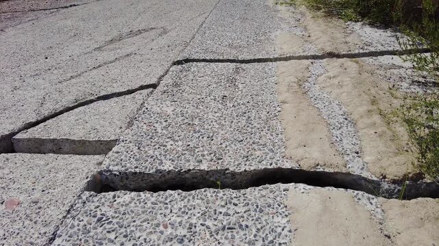 Footage shows cracks formed in the pavement and ground in a construction area. The ground is unstable and shows signs of shifting. The concrete surface has large fissures, indicating potential issues 