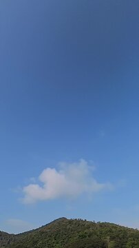 Timelapse of white clouds moving across a blue sky above a forested mountain, creating a peaceful natural landscape for nature, travel and weather concepts.