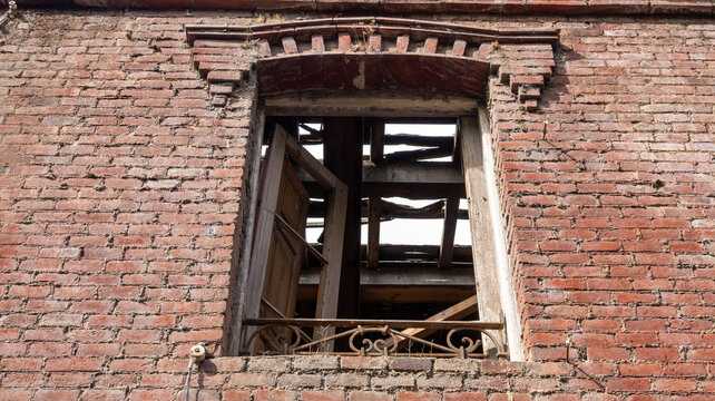 Ventana rota en muro de ladrillo rojo con techo destruido