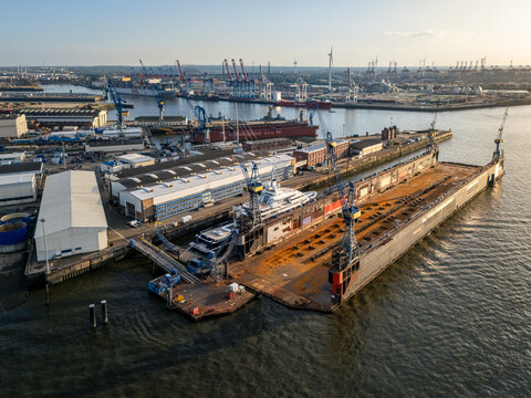 Hamburg, Germany - 24 August 2026: Aerial view of Blohm + Voss Dock 11 in the Port of Hamburg with a yacht under maintenance, industrial cranes, shipyard buildings, and the Elbe river.