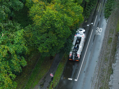 Riga, Latvia - 23 August 2026: Aerial view of emergency services clearing storm damage with a utility vehicle parked on a wet road next to fallen trees and debris in the aftermath of Storm Priska.