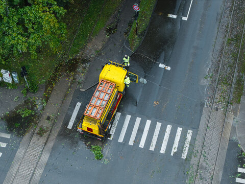 Riga, Latvia - 23 August 2026: Aerial view of emergency services clearing storm damage with a yellow truck on a road covered in debris from fallen trees.