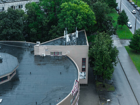 Riga, Latvia - 23 August 2026: Aerial view of a modern building with a triangular roof and a curved section, surrounded by lush green trees and a nearby road with cars.