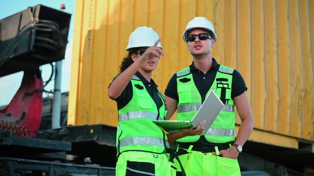 Logistics workers and engineers in safety vests using laptop while checking inventory at container terminal, representing industrial management, international trade, and supply chain technology.