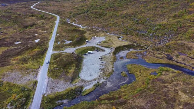 Aerial view of Slettvikane featuring a winding road crossing a small bridge over a stream, with a parking area and rugged tundra landscape in Fjord, More og Romsdal, Norway.