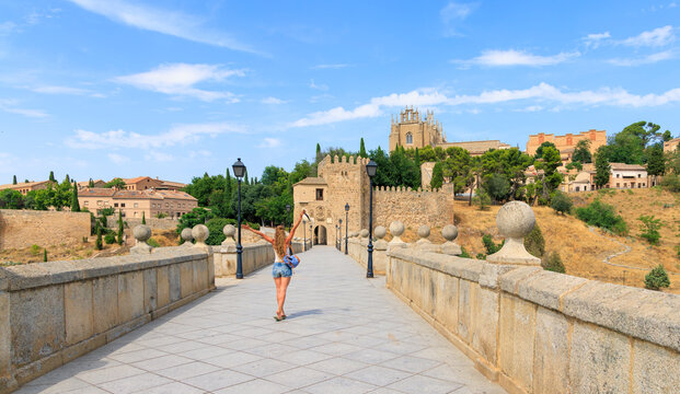 Happy woman with arms raised on historic stone bridge, San Marin in toledo, tour tourism in Spain